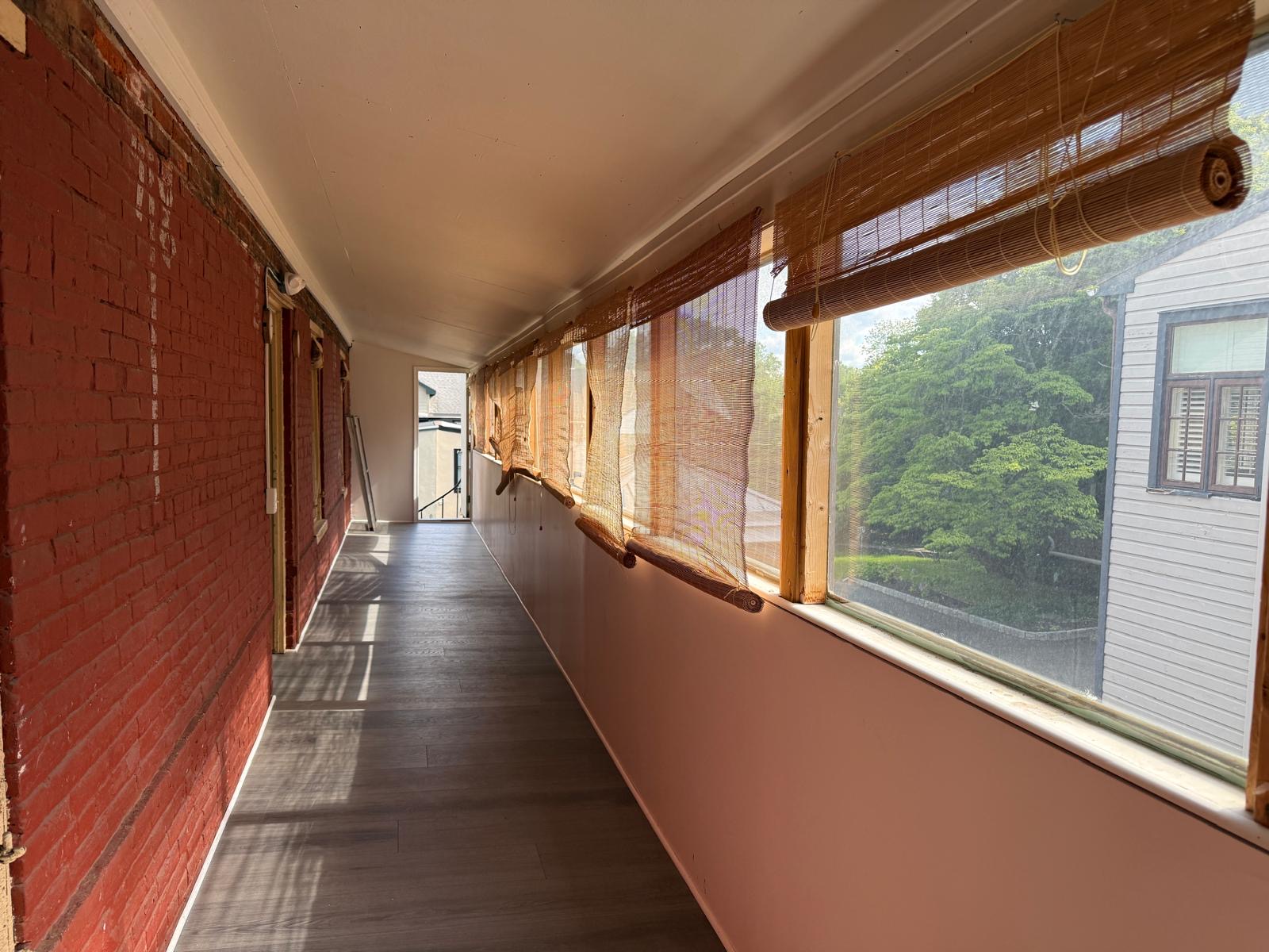 Long gallery room with red brick wall, woven window shades, and light across the floor.