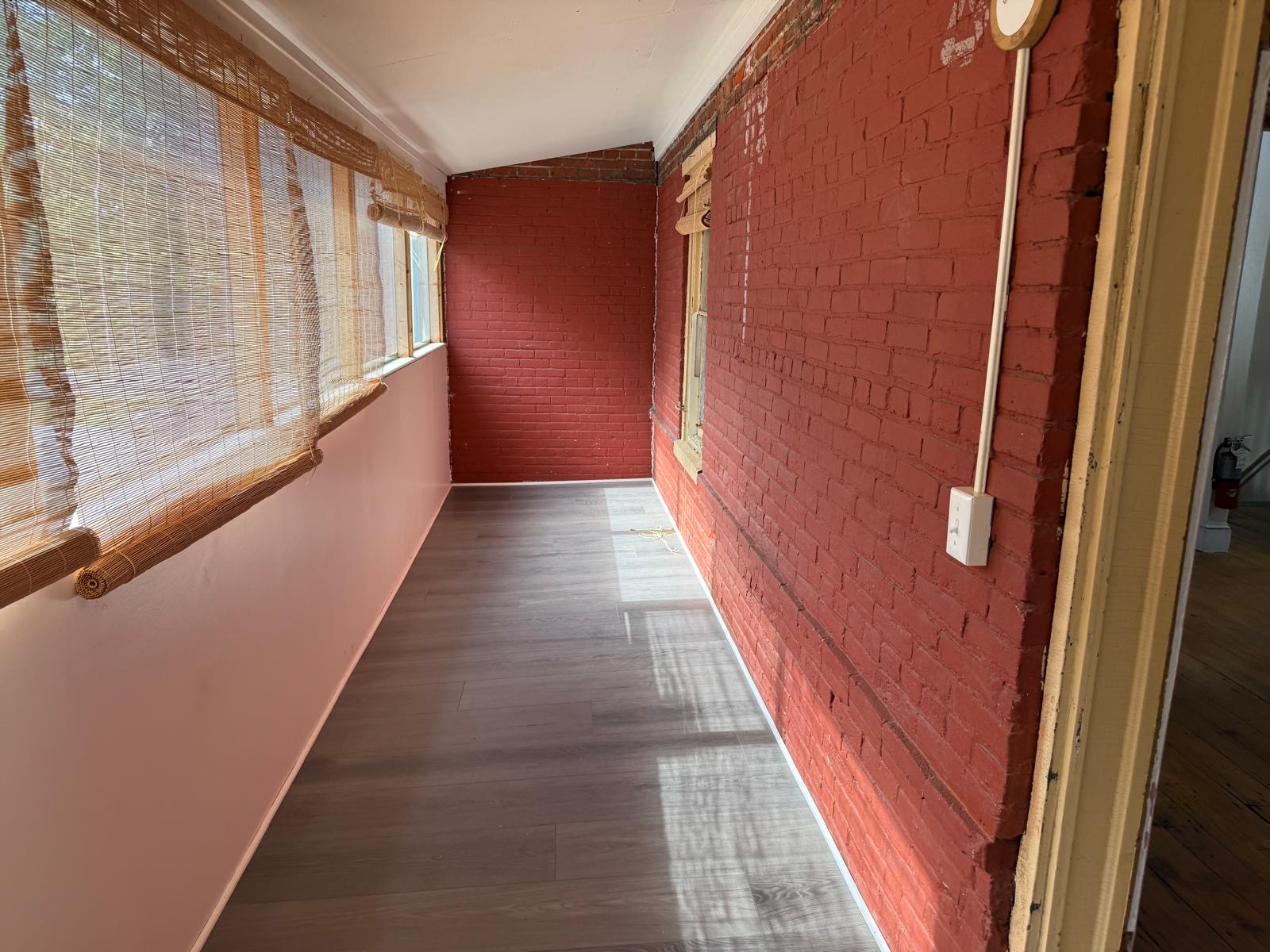 Gallery room view with red brick wall, windows, and warm filtered sunlight.