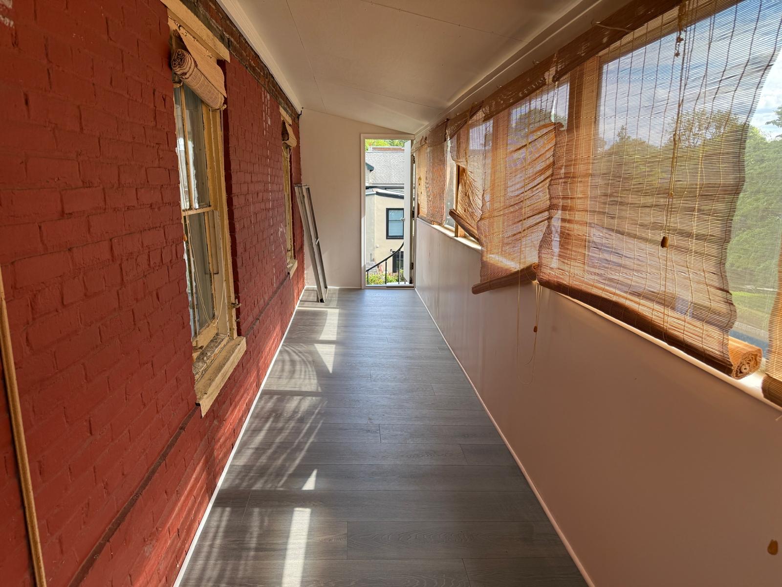 Linear gallery room with exposed red brick, large windows, and a door at the far end.