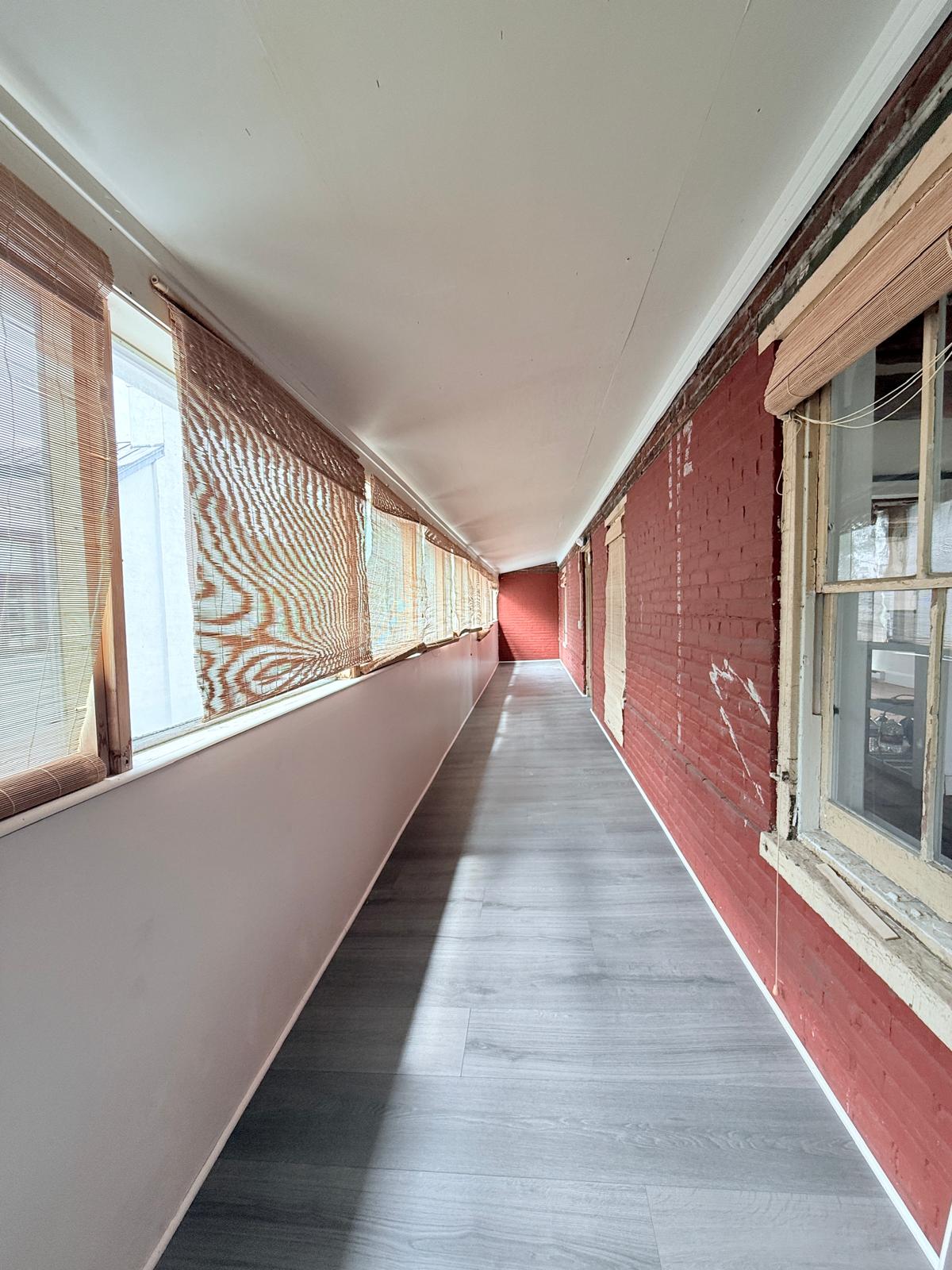Long gallery room corridor with pink-washed wall, bamboo blinds, exposed brick, and light across the floor.