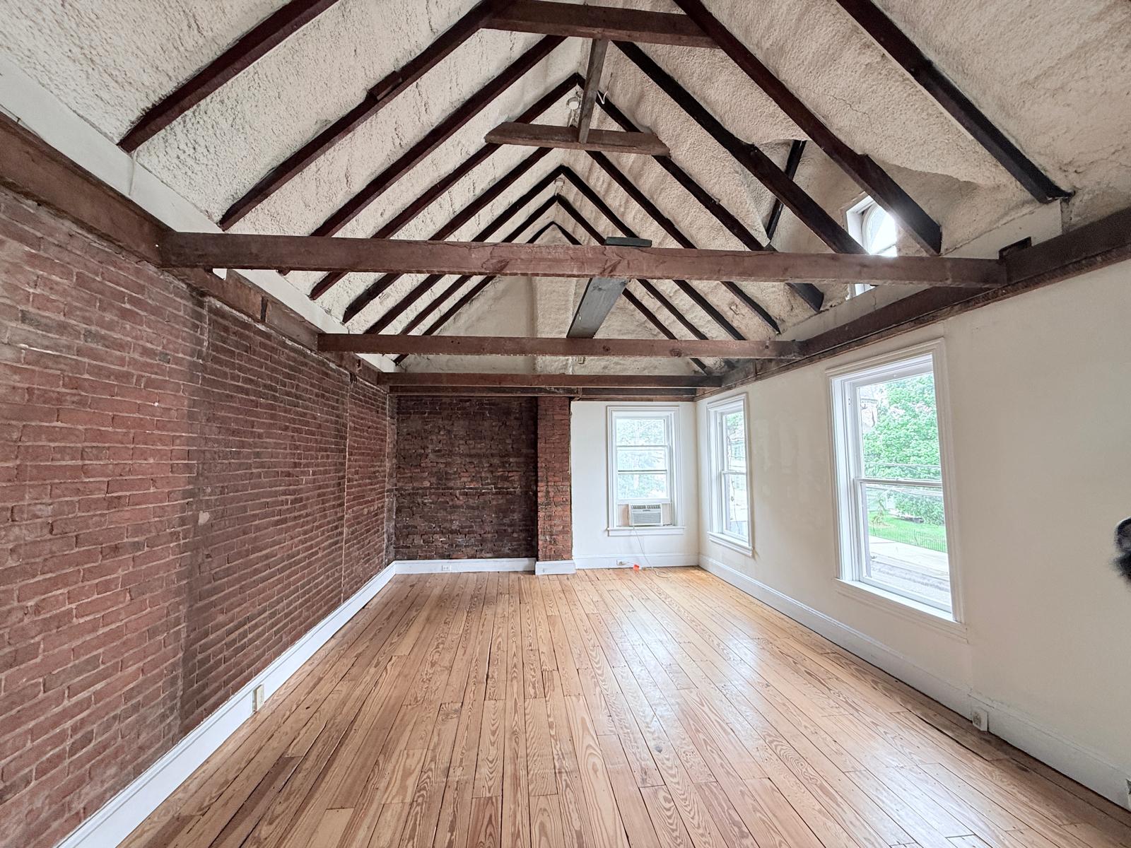 Great Hall interior with vaulted exposed beam ceiling, white walls, and original wide-plank floors.