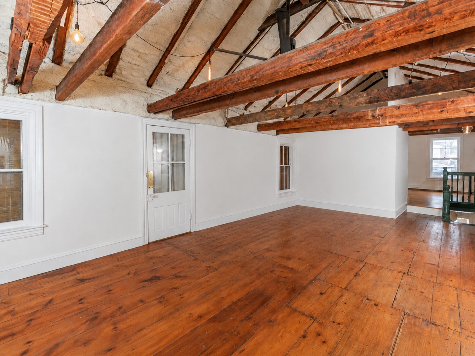 Large studio showroom with exposed timber beams, white walls, and warm wood floors.
