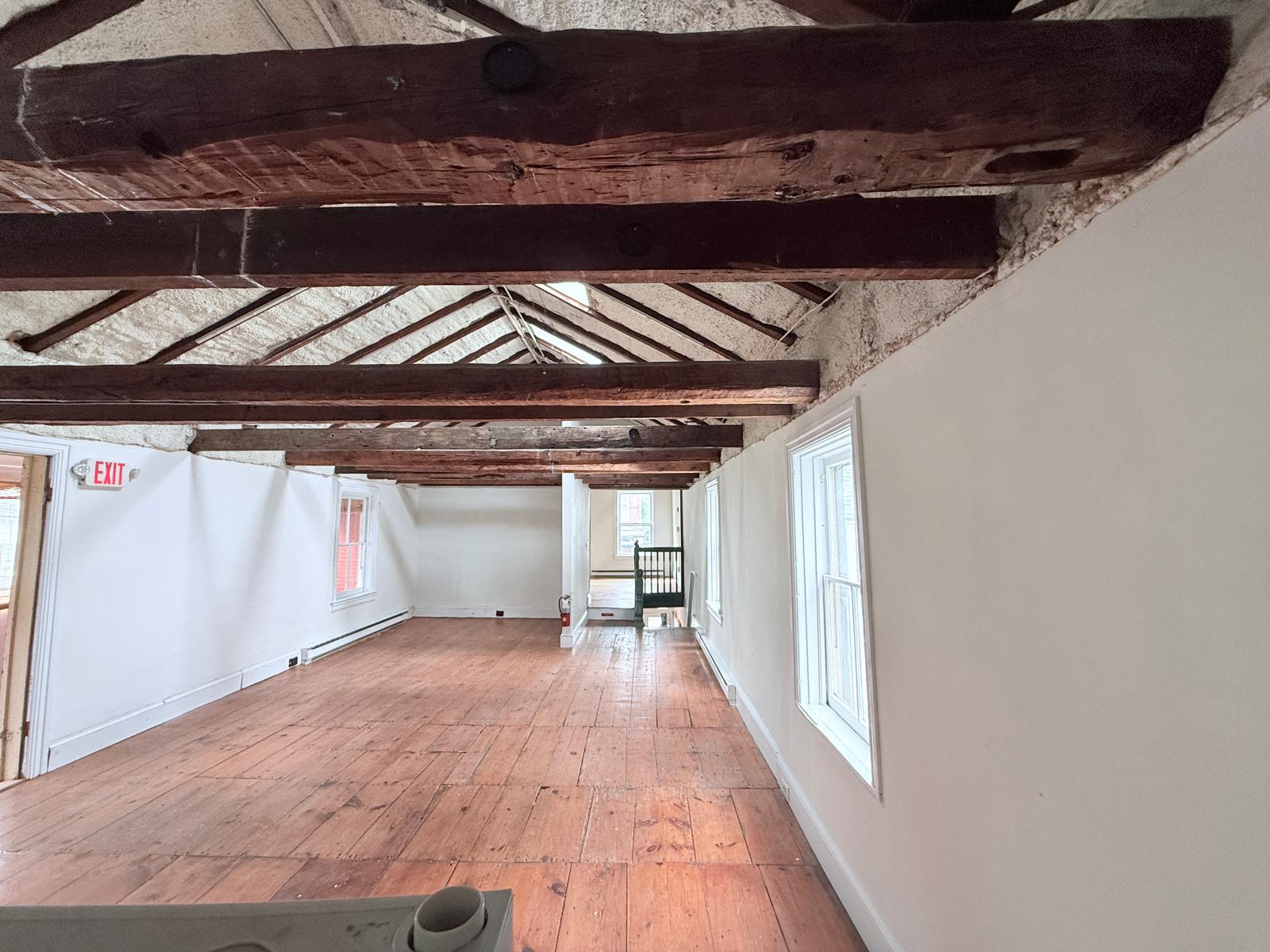 Large studio with dramatic exposed brick wall, cathedral timber ceiling, and warm hardwood floors.