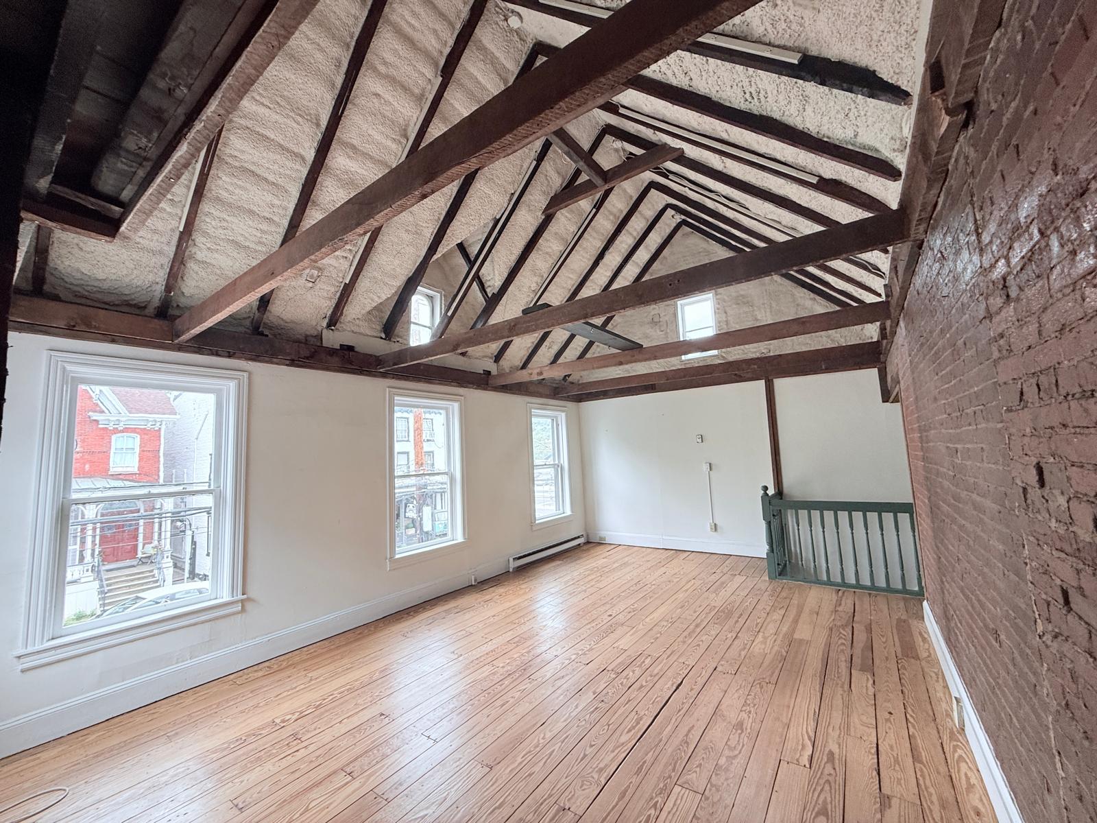 Large studio showroom with vaulted ceiling, street-facing windows, and original wood floors.