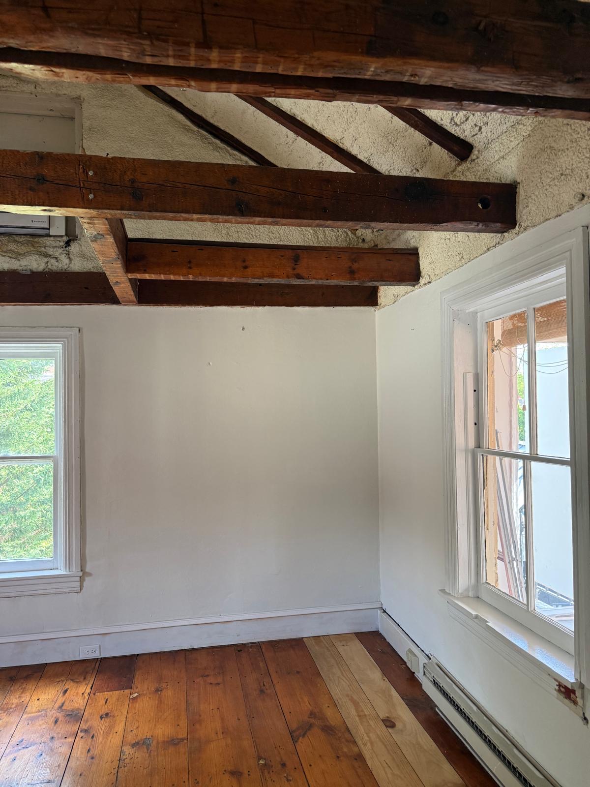 Corner of the private office with two windows, timber ceiling beams, and wood flooring.