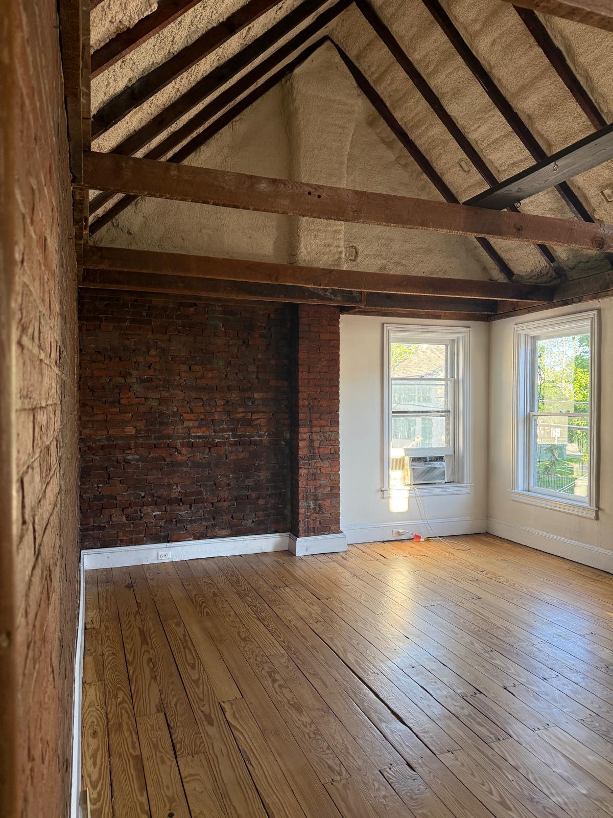 Private office studio showing exposed brick wall, vaulted timber ceiling, and natural light from two windows.