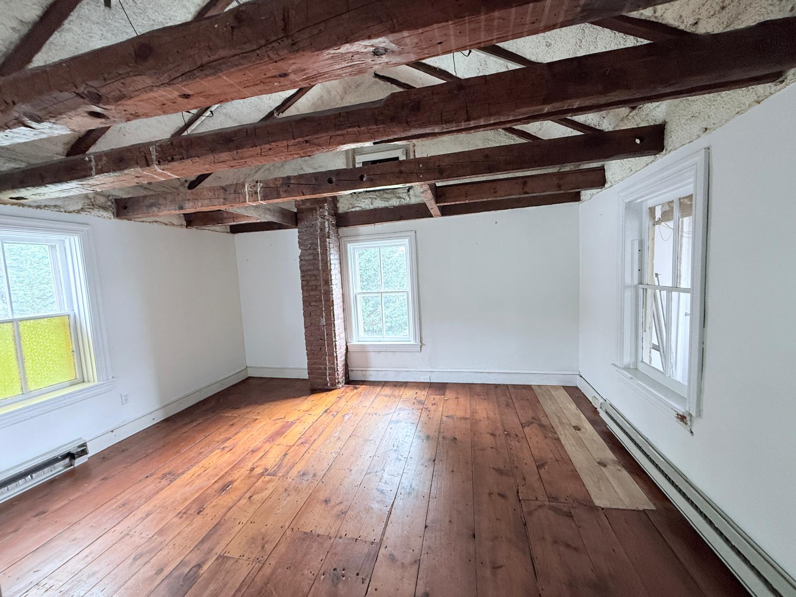 Private office studio with exposed brick column, rustic pine floors, and natural light from multiple windows.
